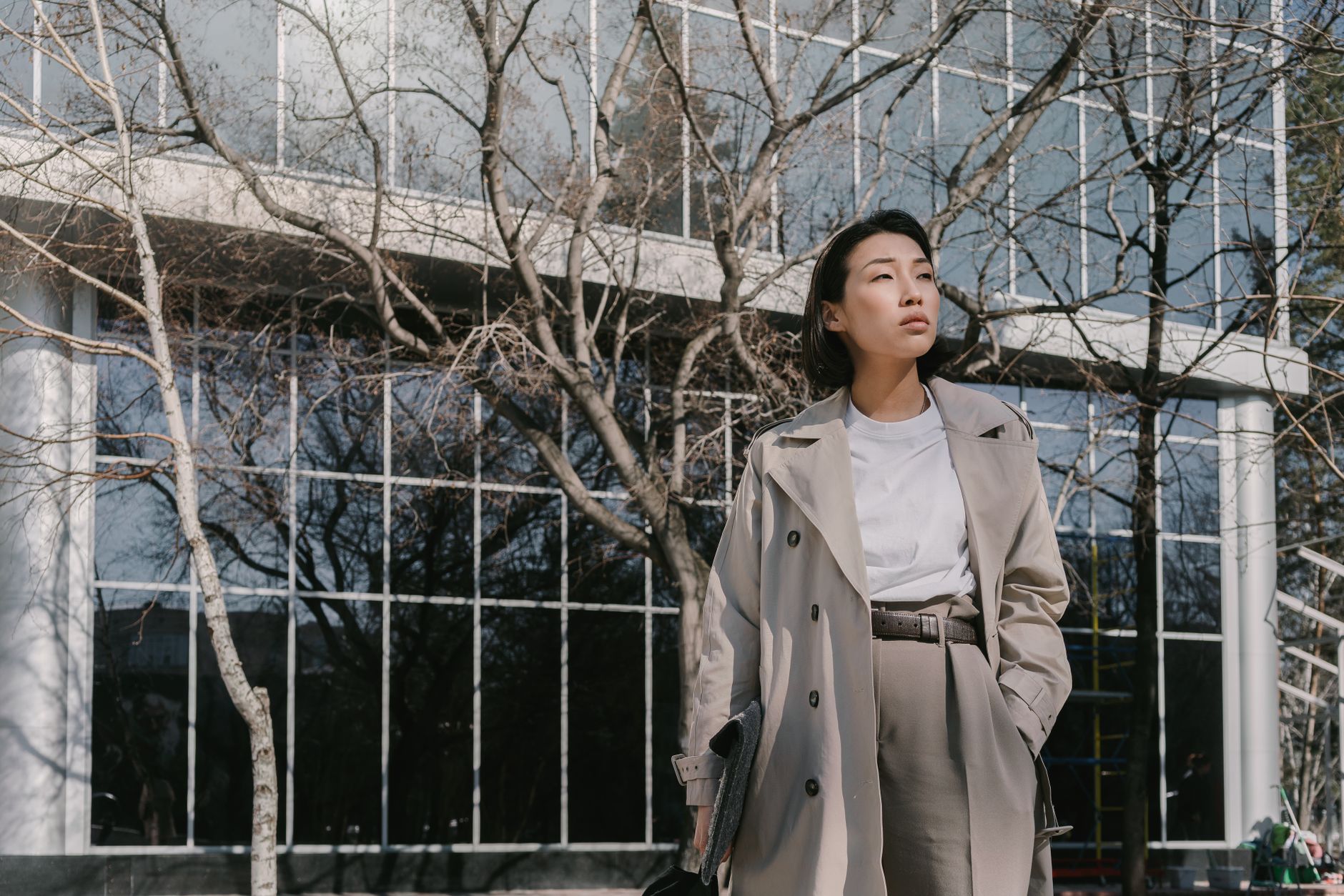 Fashionable woman in gray coat stands confidently outdoors against sleek building backdrop.