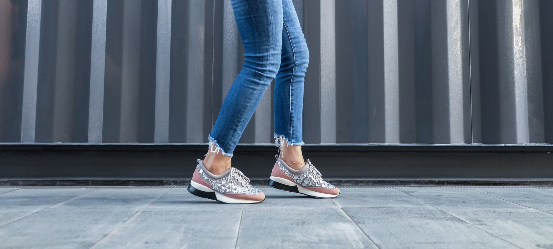 A fashionable woman walks on urban pavement in trendy denim jeans and stylish sneakers.