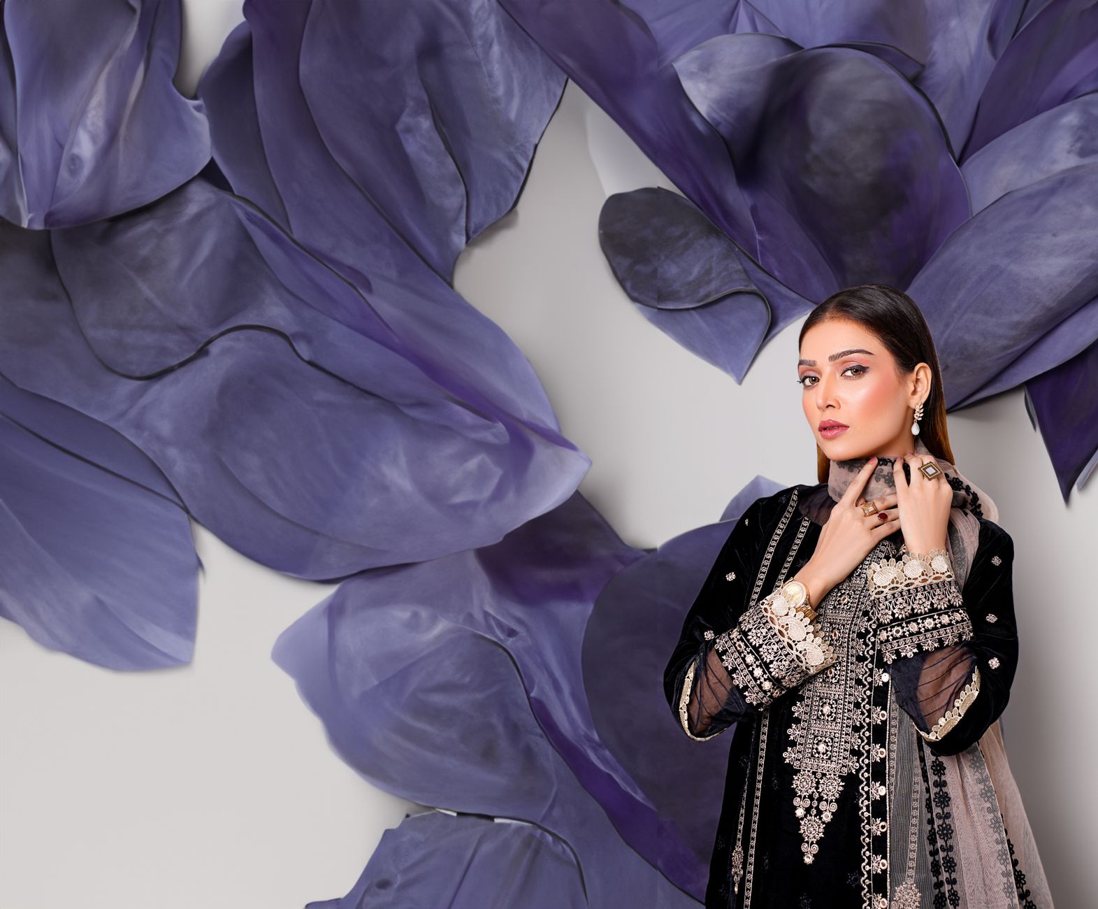 Stylish fashion model in embroidered dress poses with a vibrant artistic background.