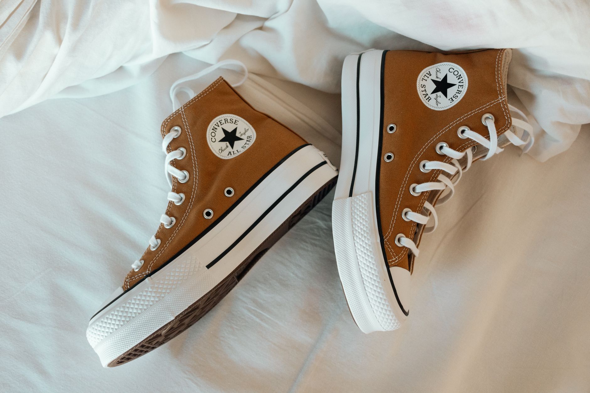 Stylish brown high top sneakers on a crisp white sheet background.