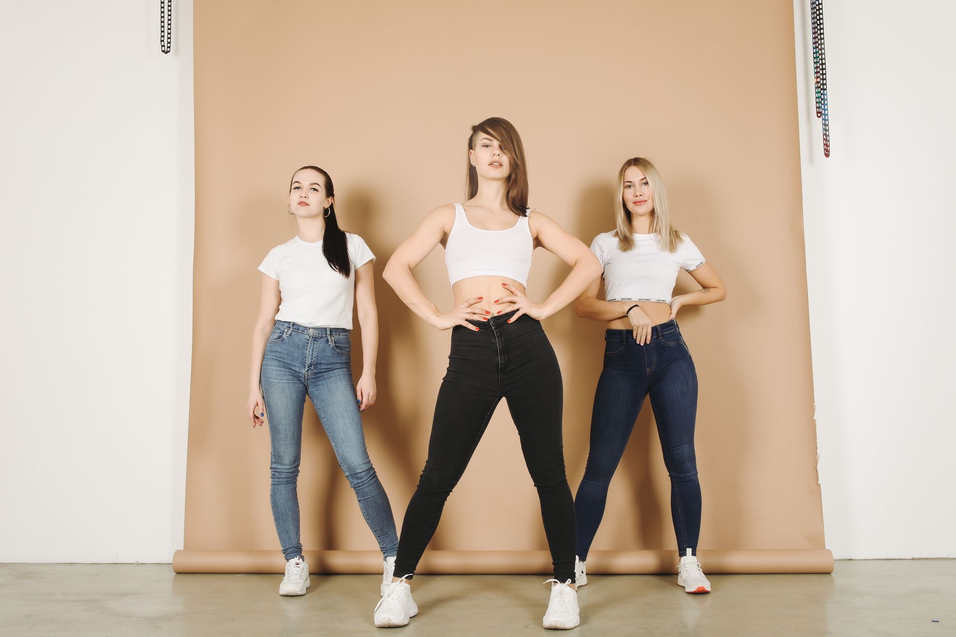 Three women in casual denim outfits posing confidently in a studio setting.