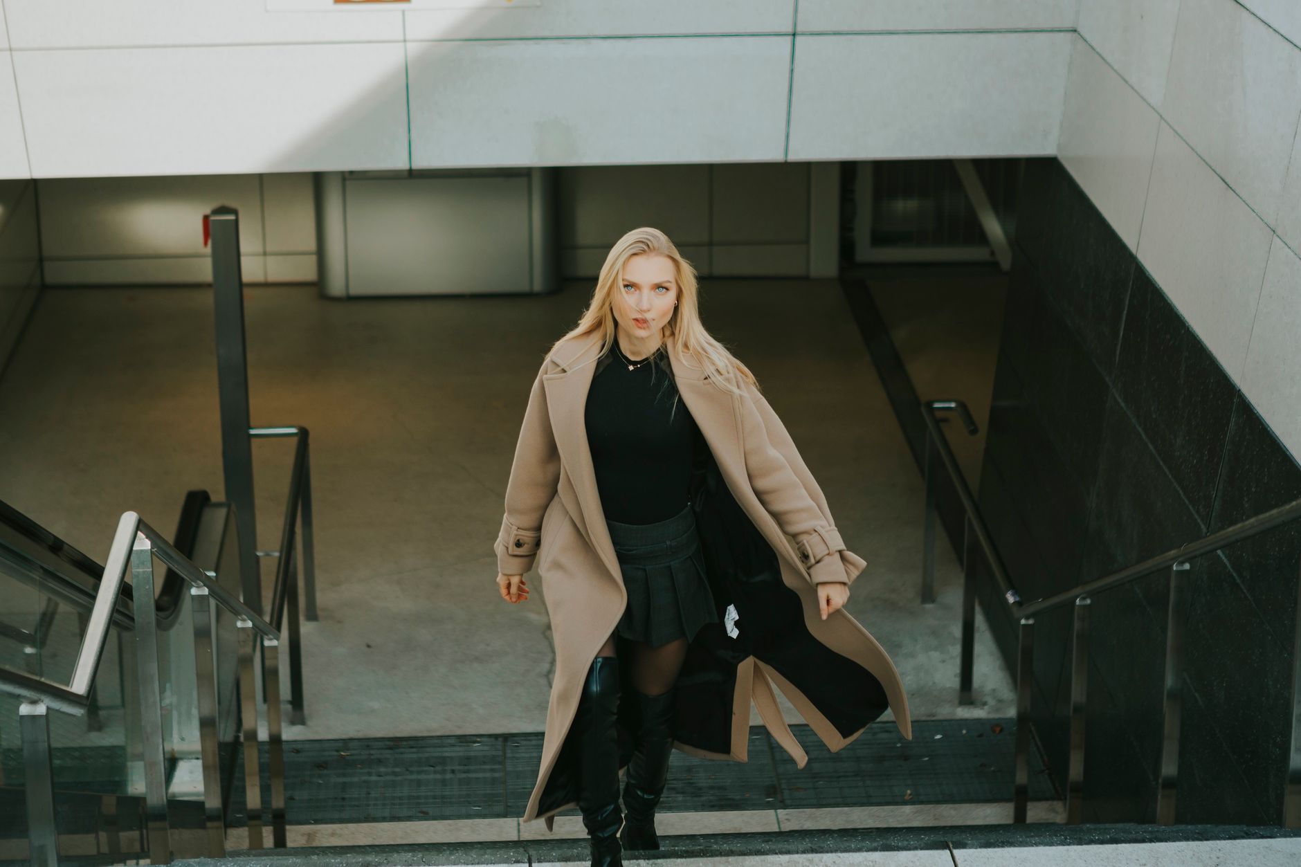 Fashionable woman in Berlin wearing a wool coat and boots, elegantly walking down steps.