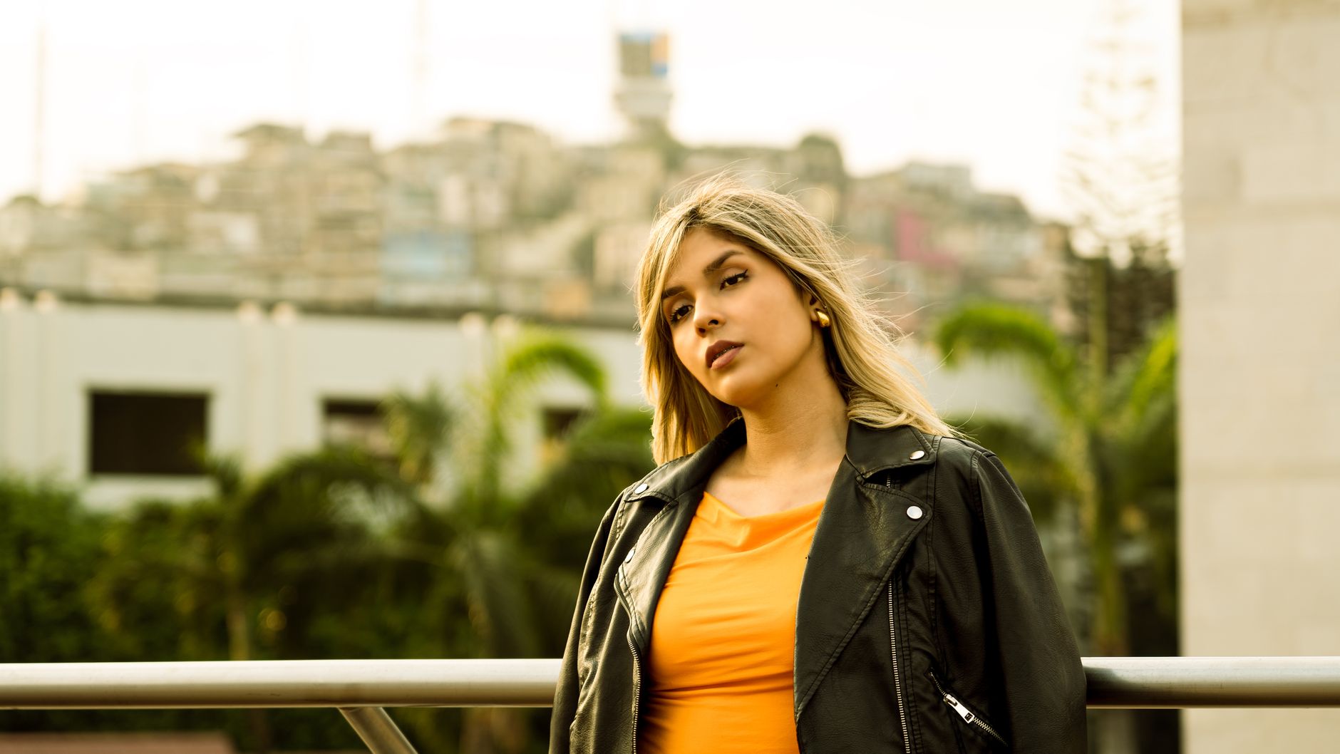 Portrait of a young woman in urban environment wearing a leather jacket and orange top.